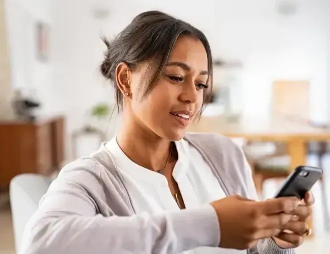 Woman smiling while looking at smartphone in bright indoor setting